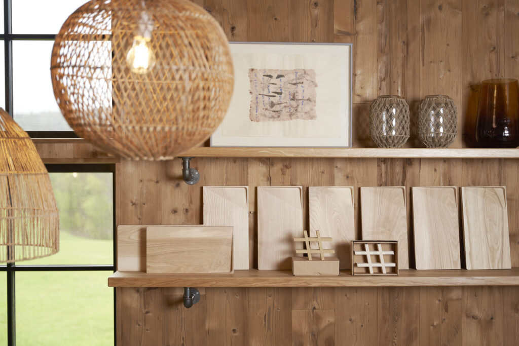 Regaldetail in einem Hofladen mit aufgereihten Holzbrettern, gerahmtem Bild und Rattanleuchten