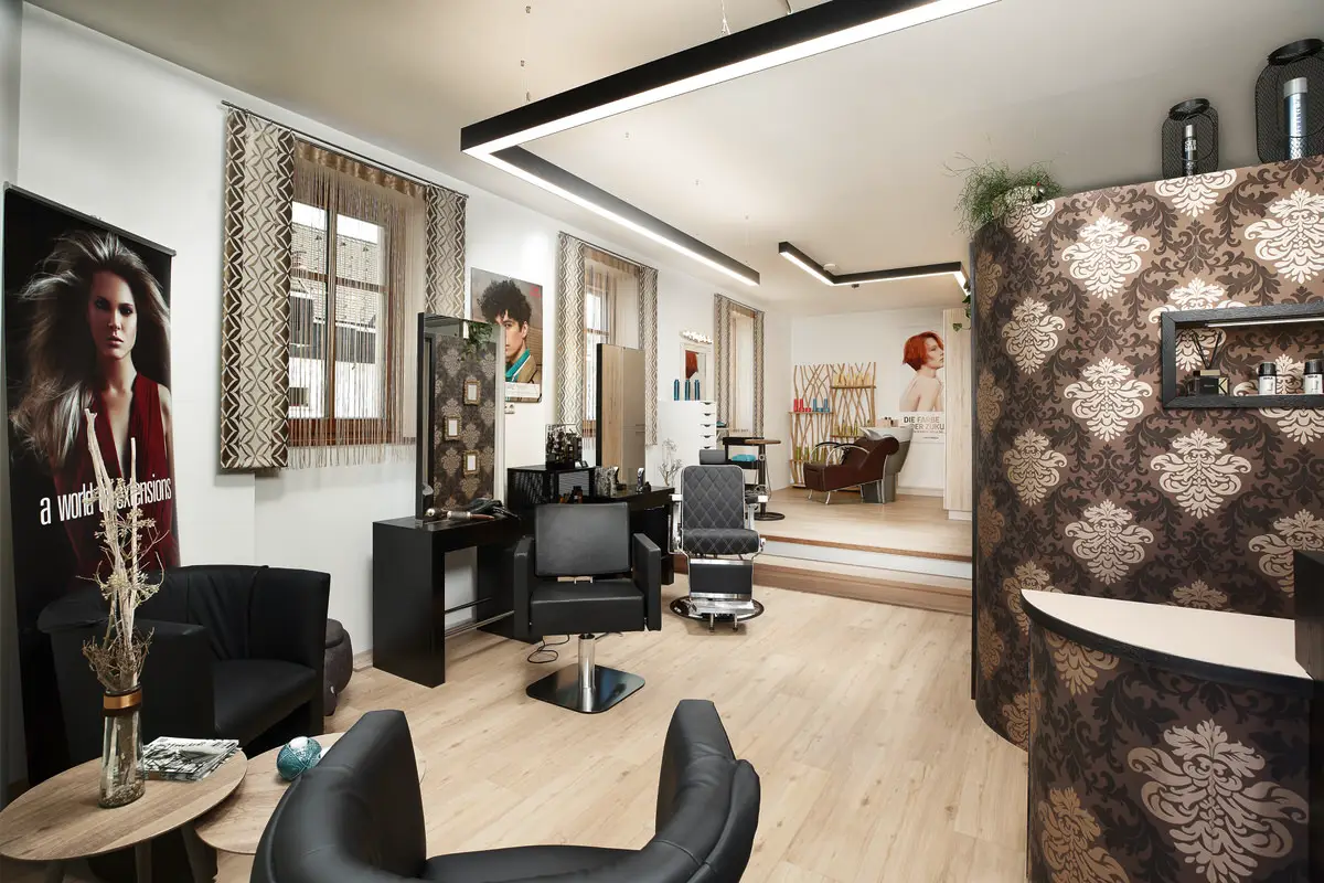 Friseursalon mit Styling-Plätzen, Spiegeln, schwarzem Friseurstuhl, Loungesesseln und gemusterter Empfangstheke