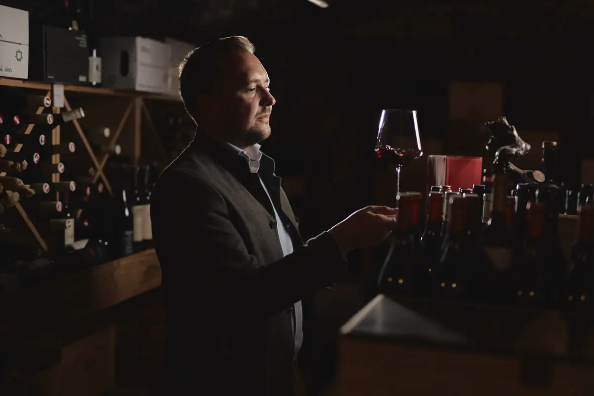 Ein Mann begutachtet im Weinkeller ein Glas Rotwein, umgeben von Weinregalen