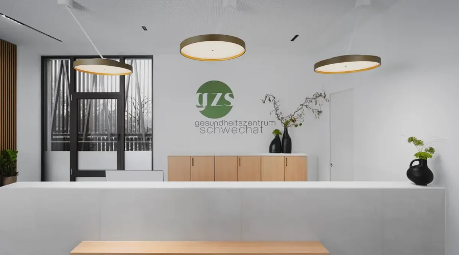 Empfangsbereich einer Praxis mit minimalistischem Tresen, runden Designleuchten und Logo an der Wand